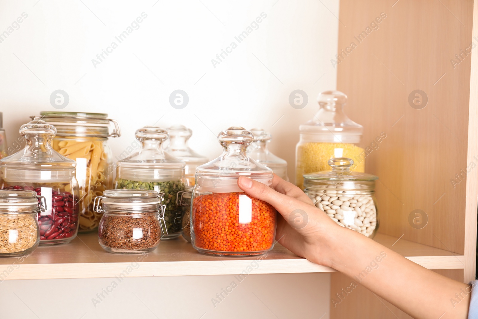 Photo of Woman taking jar of red lentil from wooden shelf, closeup