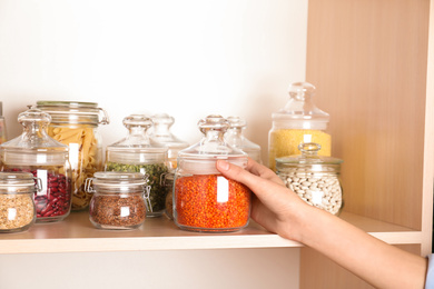 Woman taking jar of red lentil from wooden shelf, closeup