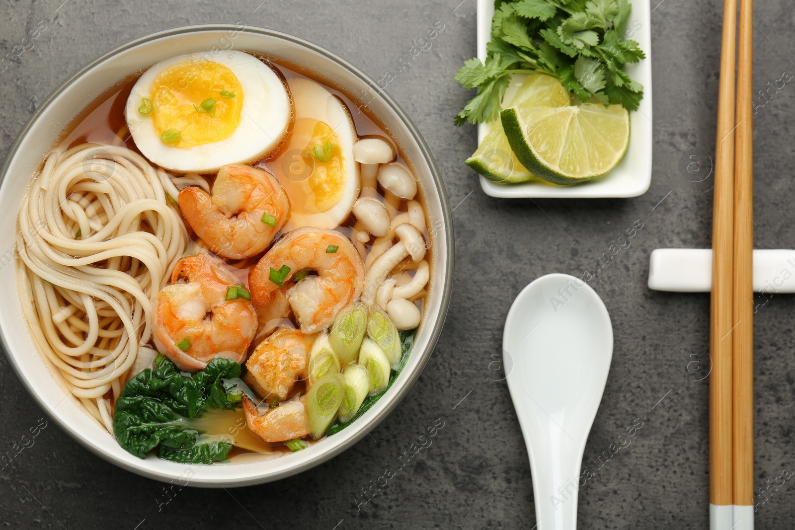 Photo of Delicious ramen with shrimps and egg in bowl served on grey table, flat lay. Noodle soup