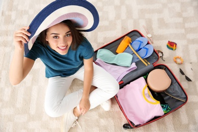 Young woman packing suitcase for summer journey at home, top view