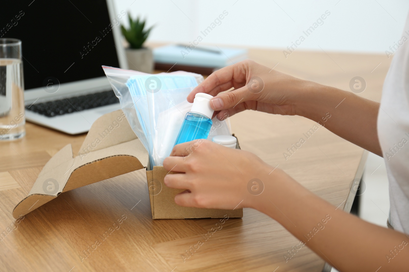 Photo of Woman unpacking box with antiseptics and respiratory masks at wooden table, closeup. Protective essentials during COVID-19 pandemic