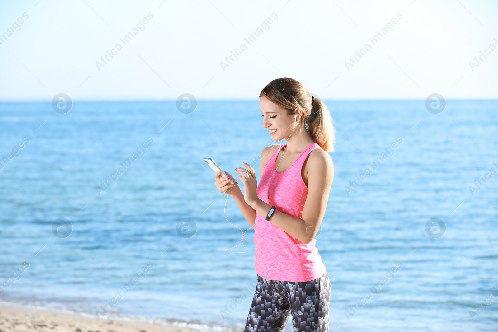 Photo of Young woman choosing music for fitness exercises on beach in morning