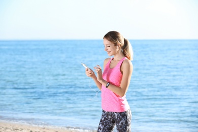 Photo of Young woman choosing music for fitness exercises on beach in morning