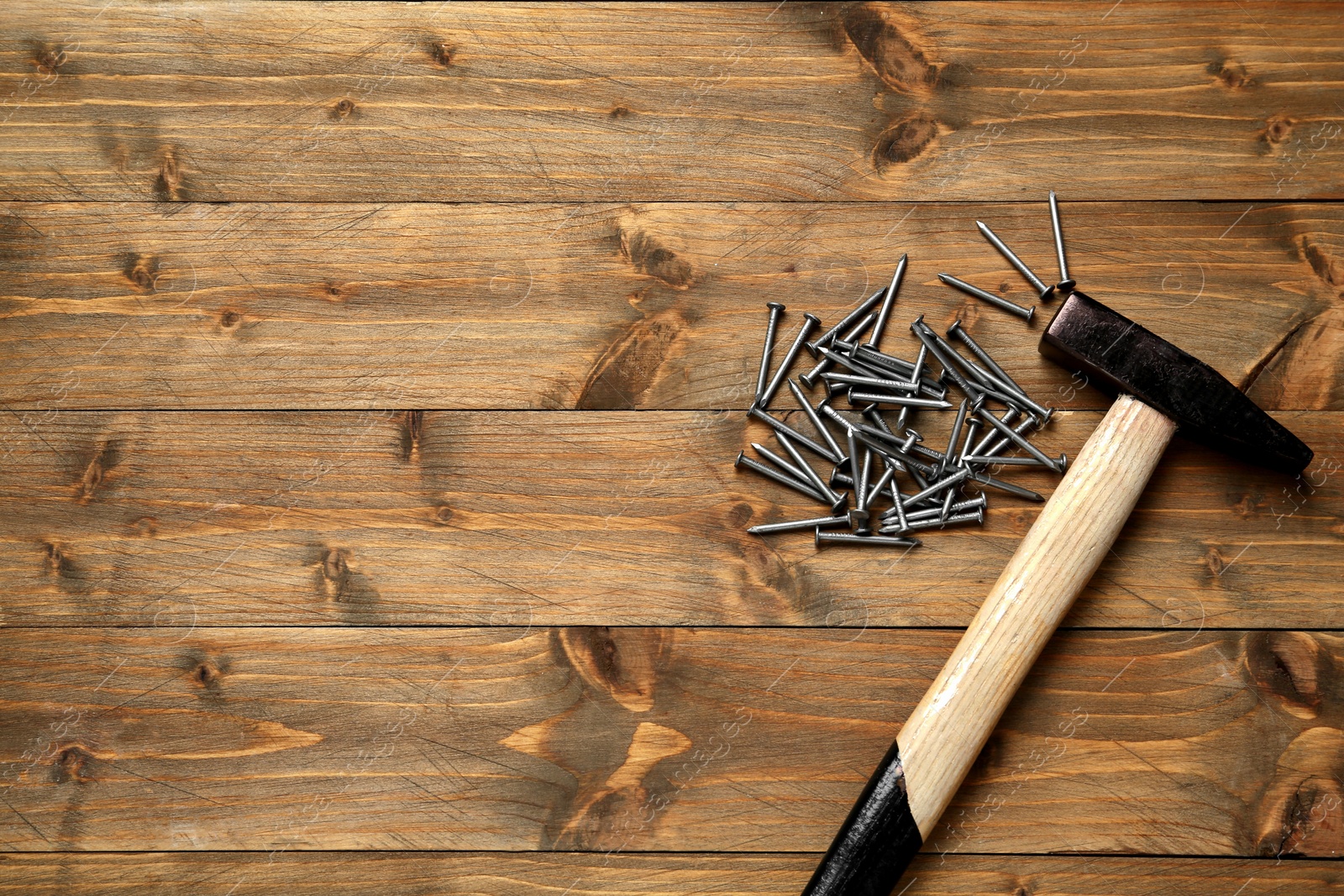 Photo of Hammer and metal nails on wooden table, flat lay. Space for text