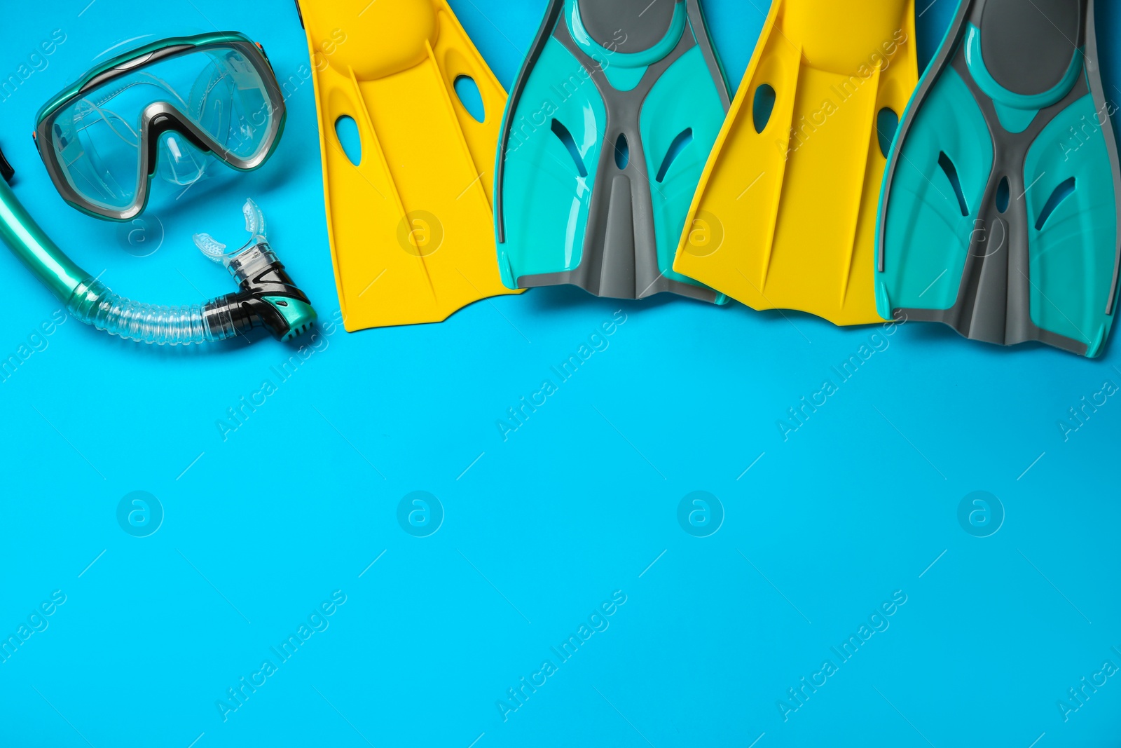 Photo of Different flippers and mask on light blue background, flat lay. Space for text