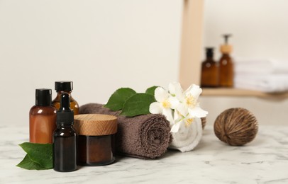 Photo of Beautiful jasmine flowers, skin care products and towels on white marble table indoors