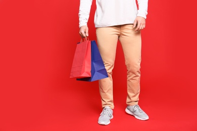 Young man with paper bags on red background, closeup. Space for text