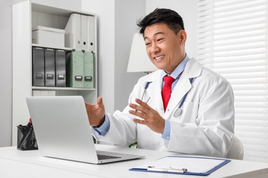 Photo of Happy doctor with laptop consulting patient at white desk in clinic. Online medicine