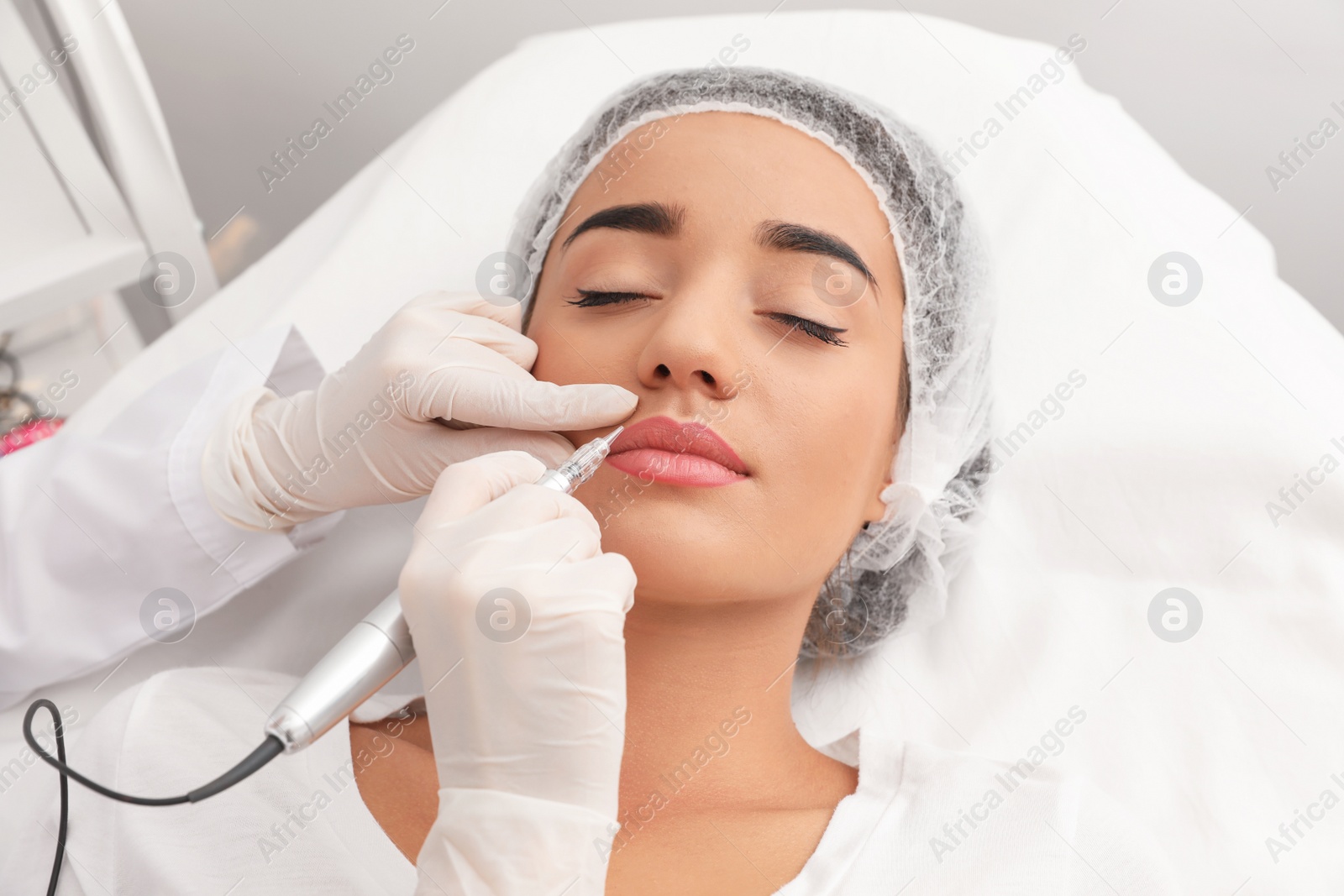 Photo of Young woman undergoing procedure of permanent lip makeup in tattoo salon