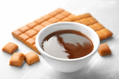 Delicious caramel candies and sauce on light background