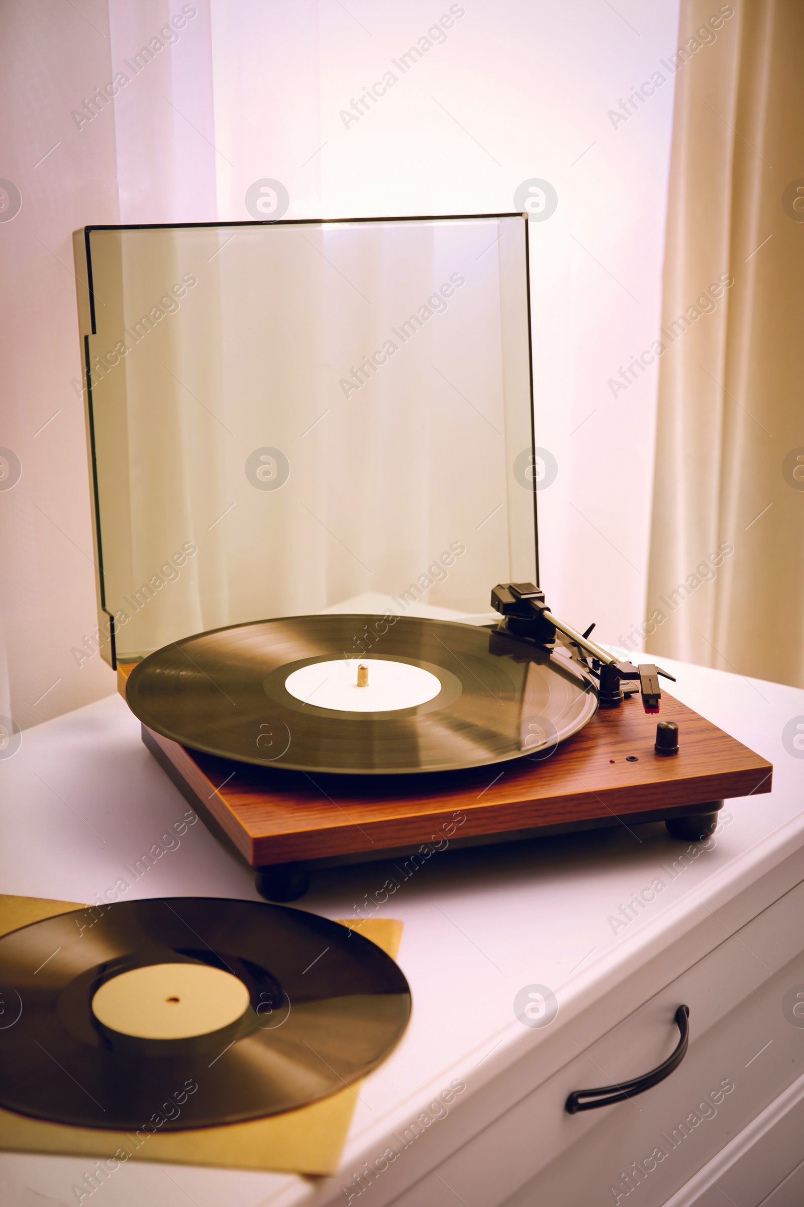 Image of Stylish turntable and vinyl records on white chest of drawers indoors
