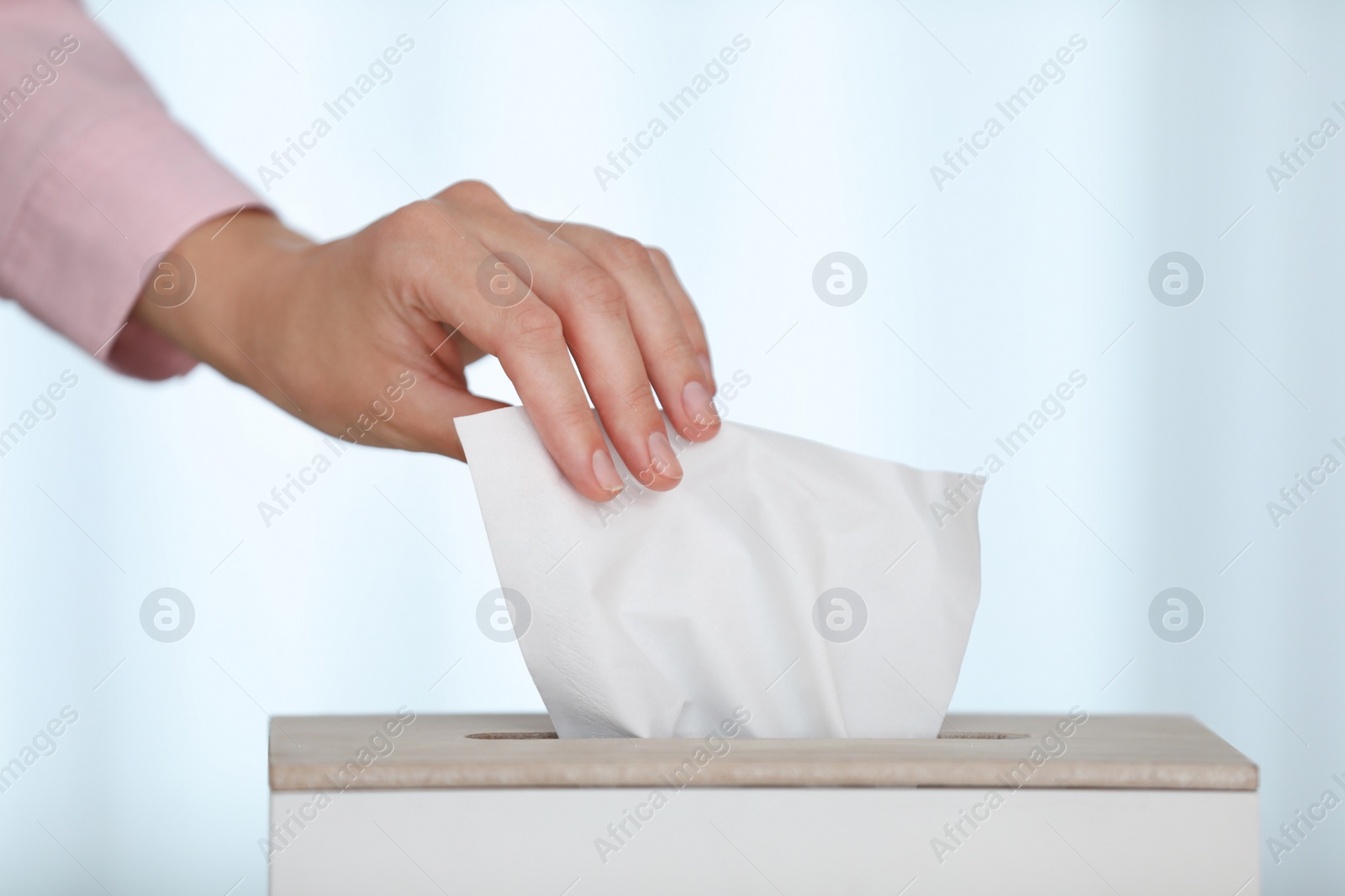 Photo of Woman taking paper tissue from holder on light background, closeup