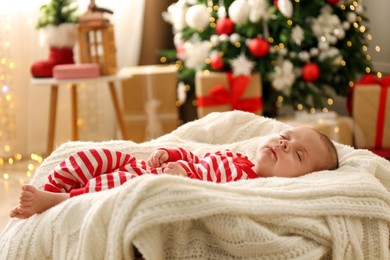 Photo of Cute little baby sleeping on knitted blanket in room decorated for Christmas