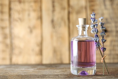 Bottle of natural essential oil and lavender flowers on wooden background. Space for text