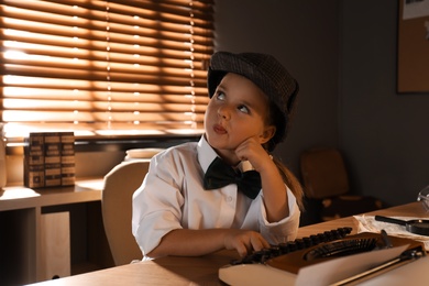 Cute little detective using typewriter at table in office