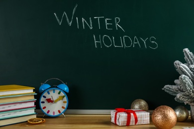 Photo of Text Winter Holidays on chalkboard near wooden table with Christmas decor and books