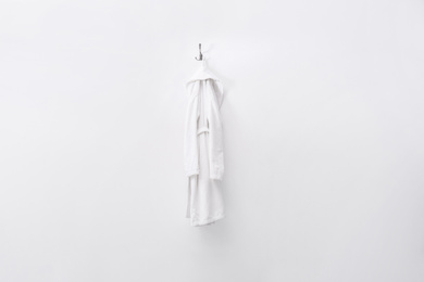 Photo of Fresh white bathrobe hanging on light wall