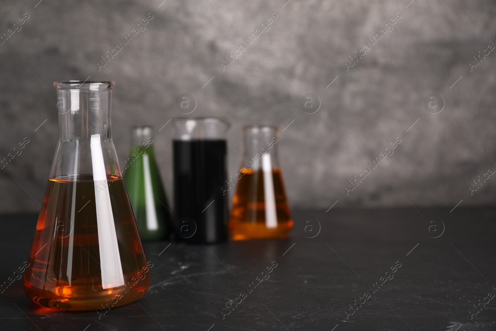 Photo of Beaker and flasks with different types of oil on grey textured table, space for text