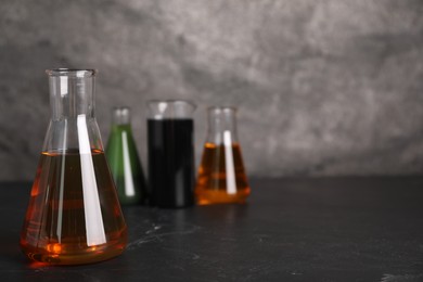 Beaker and flasks with different types of oil on grey textured table, space for text