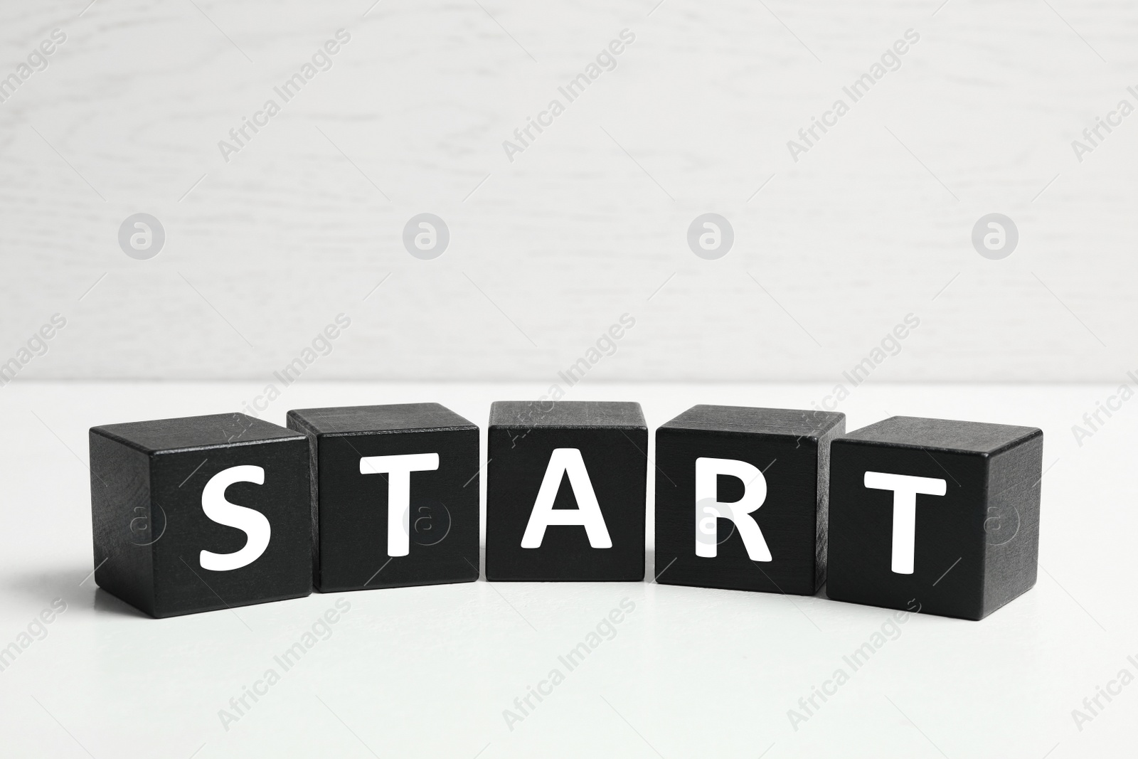 Photo of Word START made with black cubes on white table, closeup