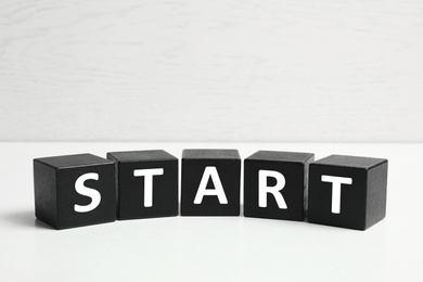 Photo of Word START made with black cubes on white table, closeup