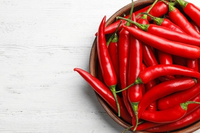 Photo of Wooden bowl with red hot chili peppers on white table, top view. Space for text