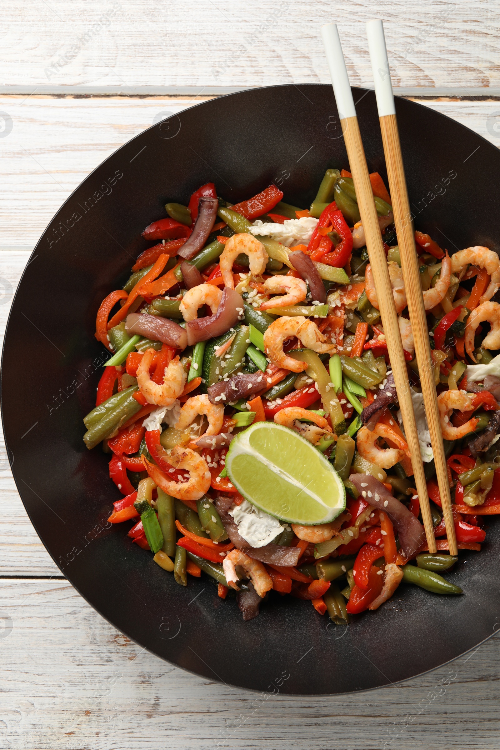 Photo of Shrimp stir fry with vegetables in wok and chopsticks on light wooden table, top view