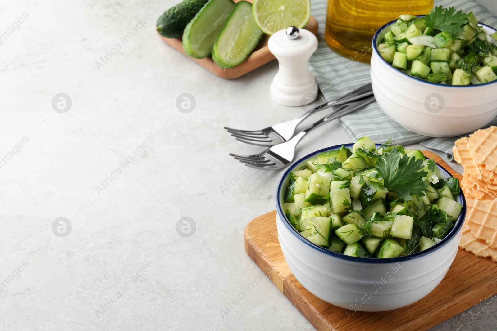 Photo of Bowl of delicious cucumber salad served on light table. Space for text