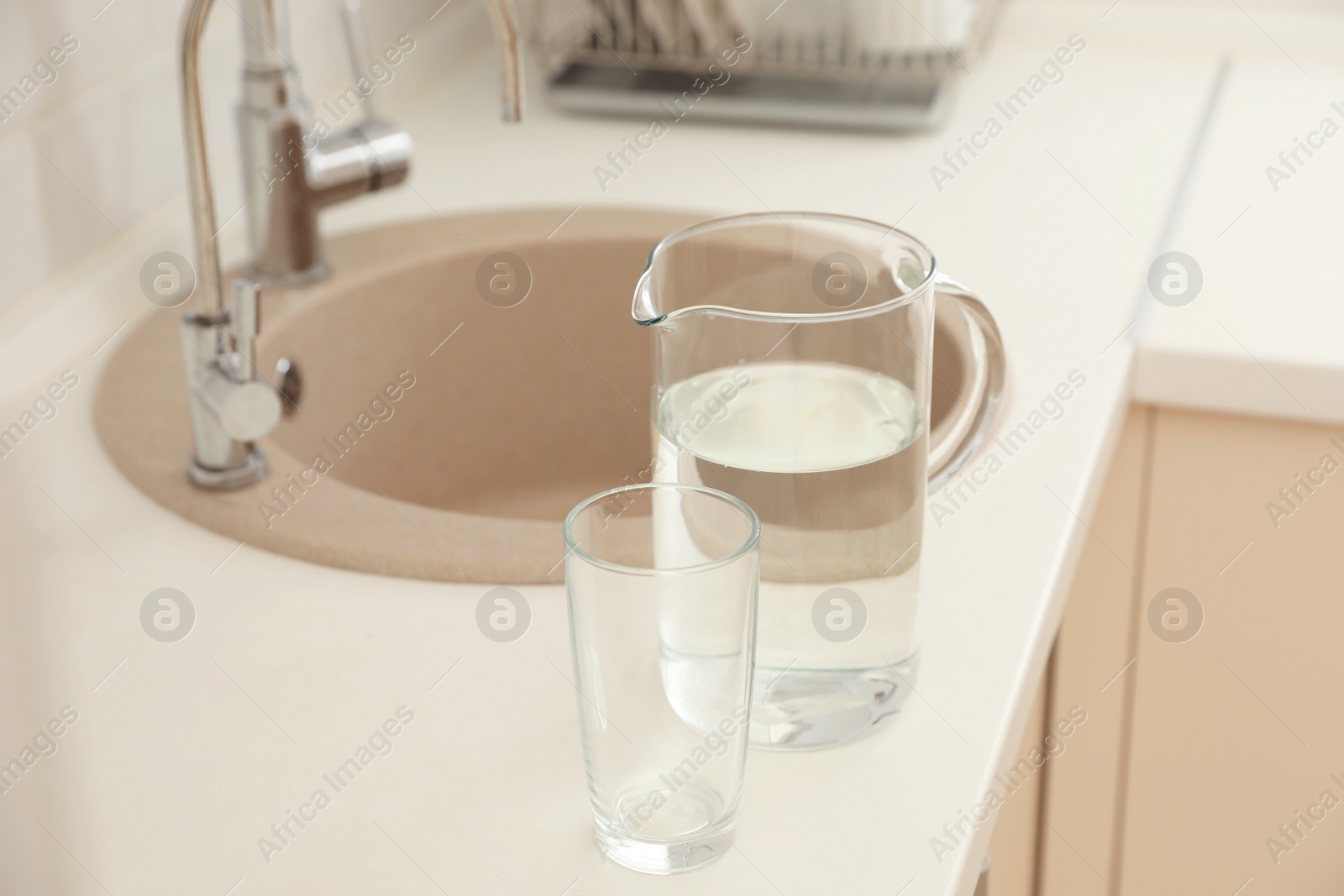 Photo of Jug and glass with water on table in kitchen