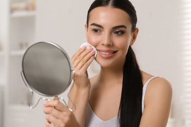 Photo of Beautiful woman removing makeup with cotton pad indoors