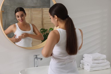 Photo of Beautiful young woman doing breast self-examination near mirror in bathroom