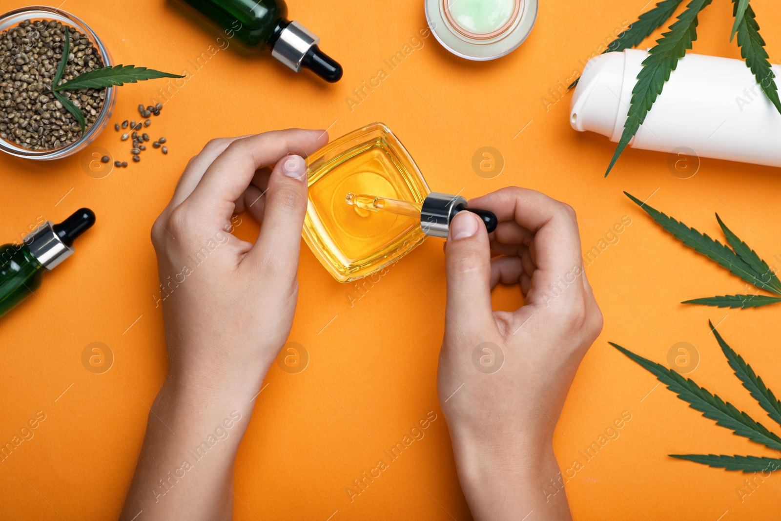 Photo of Woman dripping hemp oil into bowl on orange background, top view. Natural cosmetics