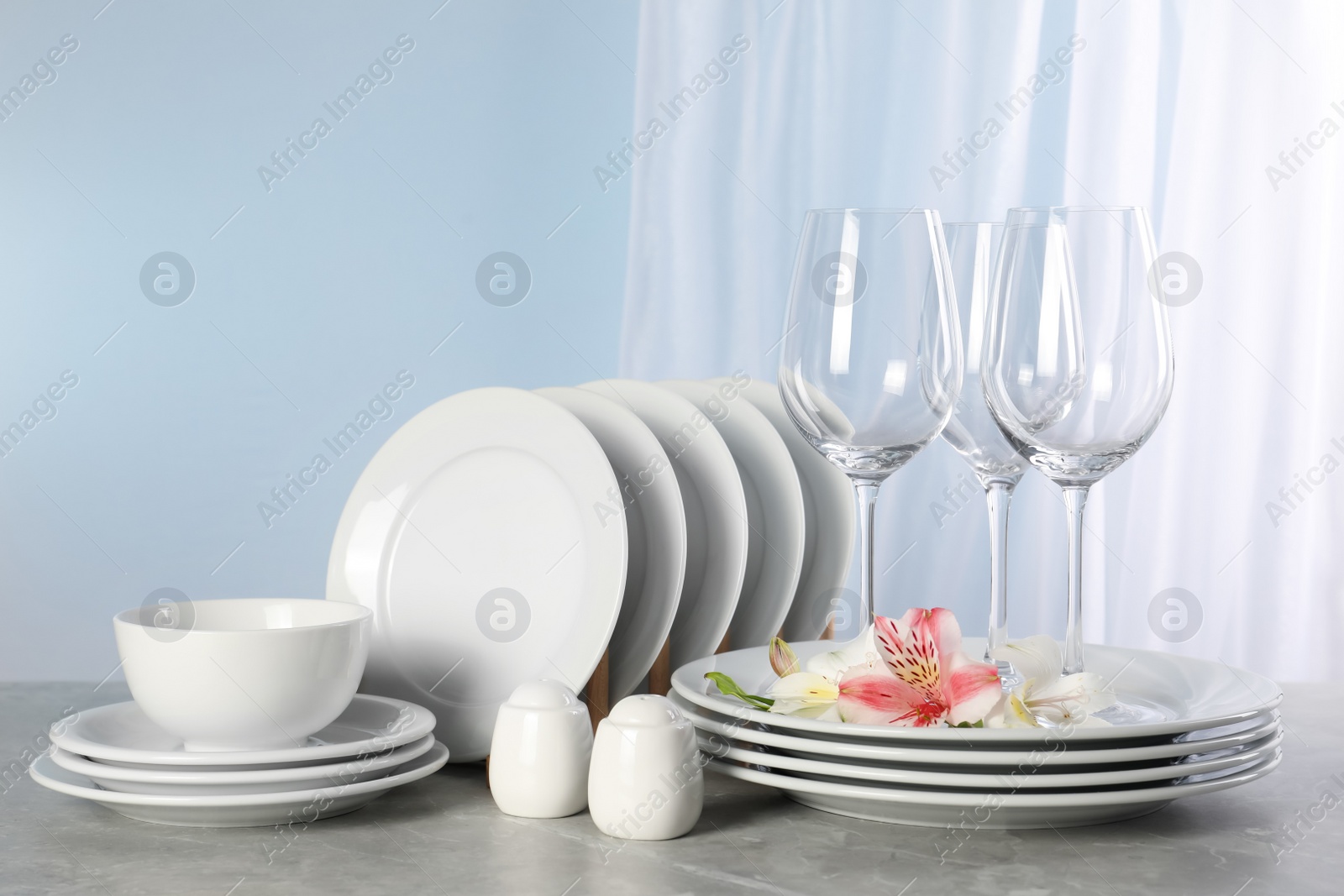 Photo of Glasses and clean dishware with flowers on grey marble table