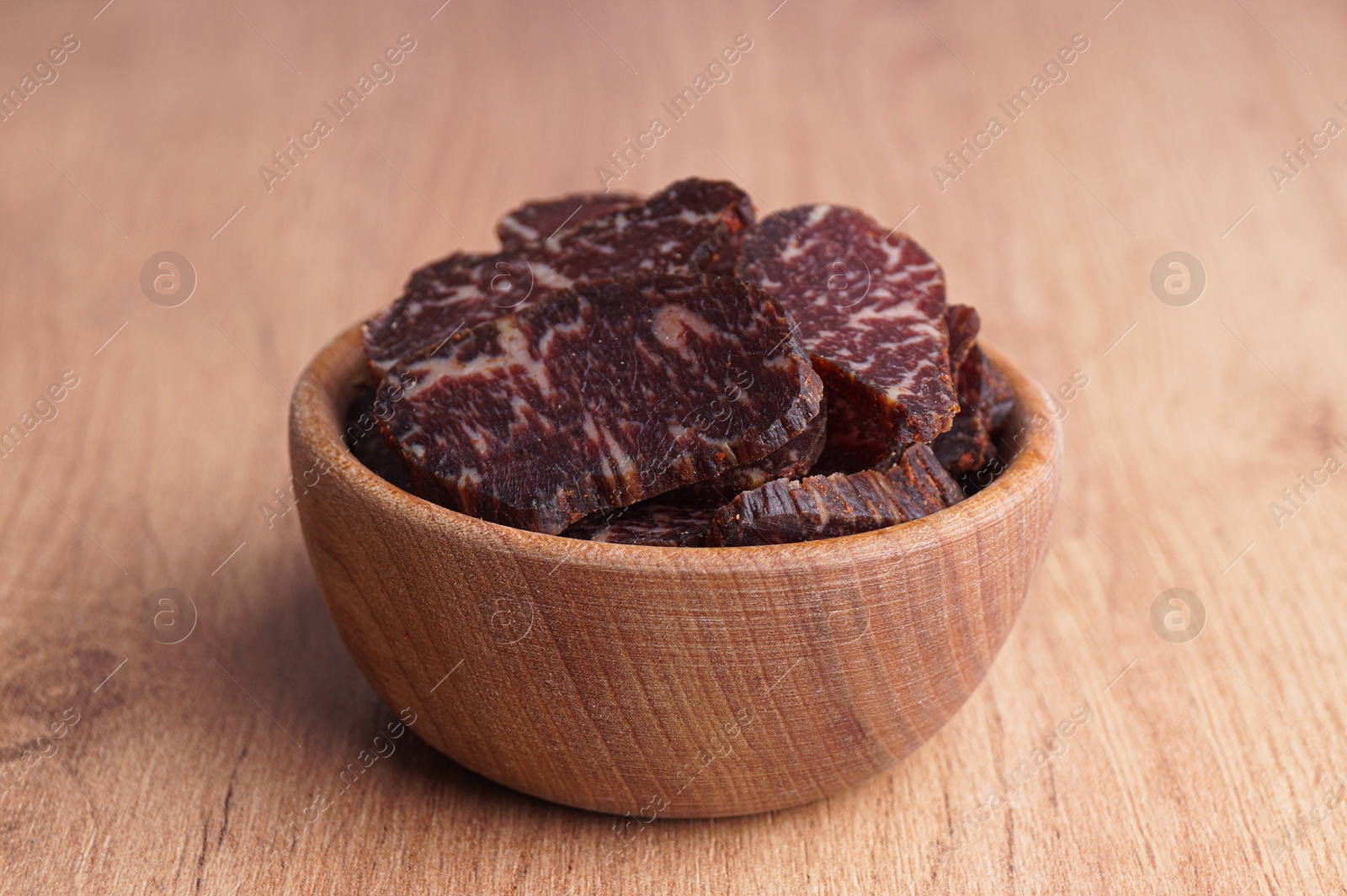 Photo of Delicious beef jerky in bowl on wooden table, closeup