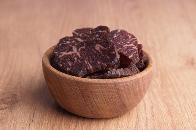 Photo of Delicious beef jerky in bowl on wooden table, closeup