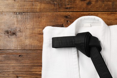 Black karate belt and white kimono on wooden background, top view. Space for text