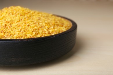 Photo of Bowl of uncooked bulgur on wooden table, closeup