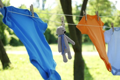 Photo of Colorful baby onesies and toy bear hanging on clothes line outside