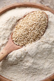 Photo of Wooden spoon with seeds on quinoa flour in bowl, top view