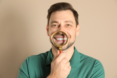 Smiling man with perfect teeth and magnifier on color background