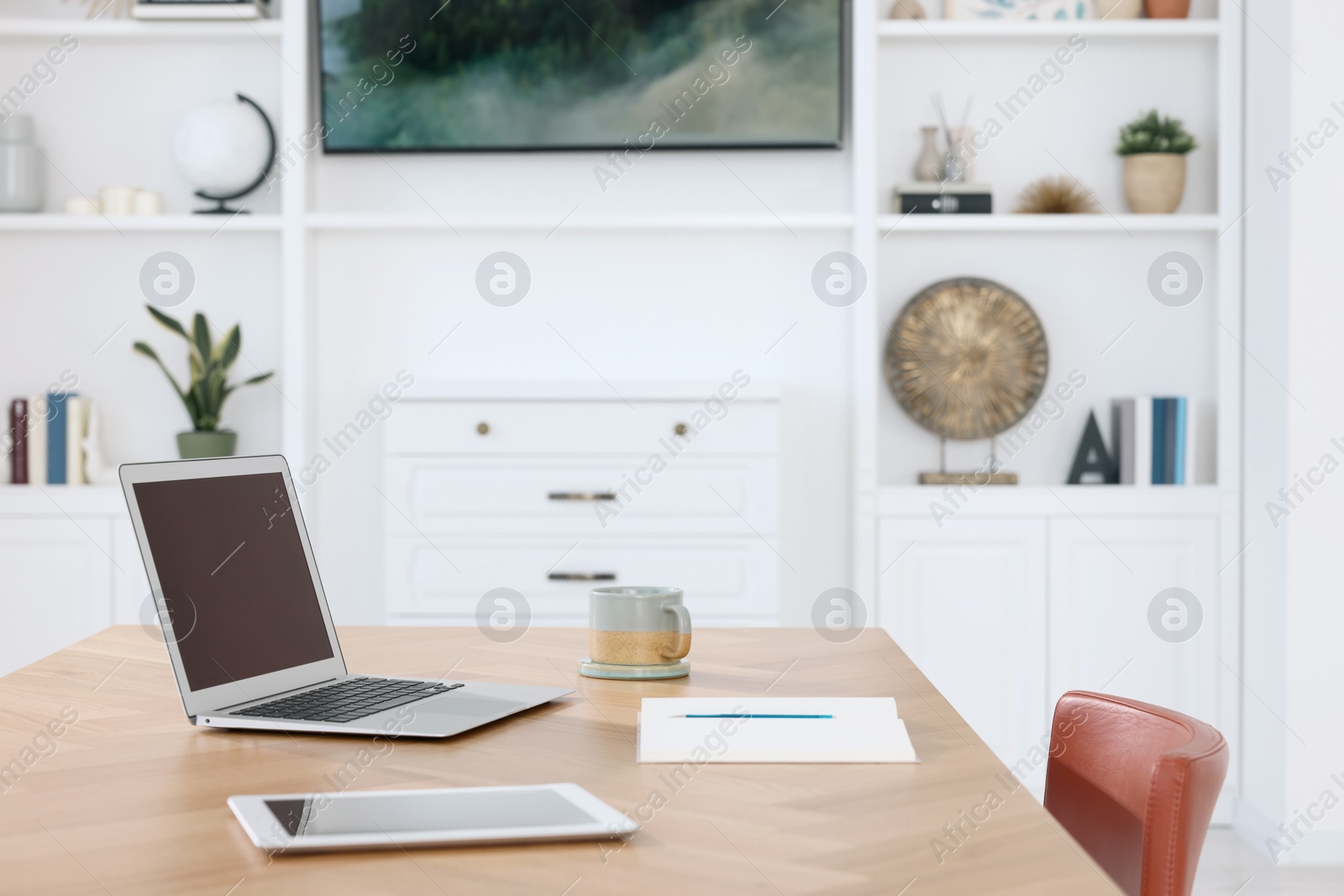 Photo of Interior design. Cosy workplace with laptop, tablet and cup on wooden table near tv area. Space for text