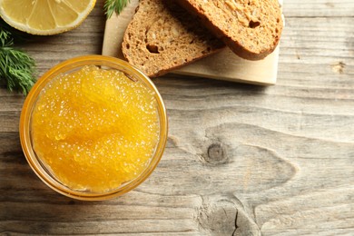 Photo of Fresh pike caviar in bowl, lemon and bread on wooden table, flat lay. Space for text