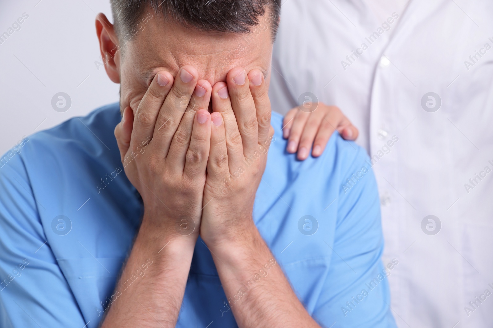 Photo of Doctor covering his face with hands while colleague comforting him in hospital, closeup