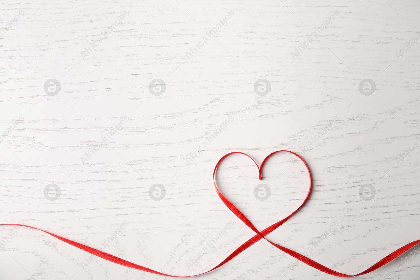 Photo of Heart made of red ribbon on white wooden background, top view with space for text. Valentine's day celebration