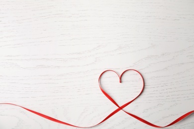 Photo of Heart made of red ribbon on white wooden background, top view with space for text. Valentine's day celebration