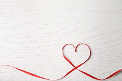 Heart made of red ribbon on white wooden background, top view with space for text. Valentine's day celebration