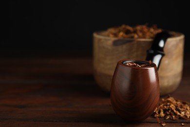 Photo of Smoking pipe and dry tobacco on wooden table against dark background, closeup. Space for text