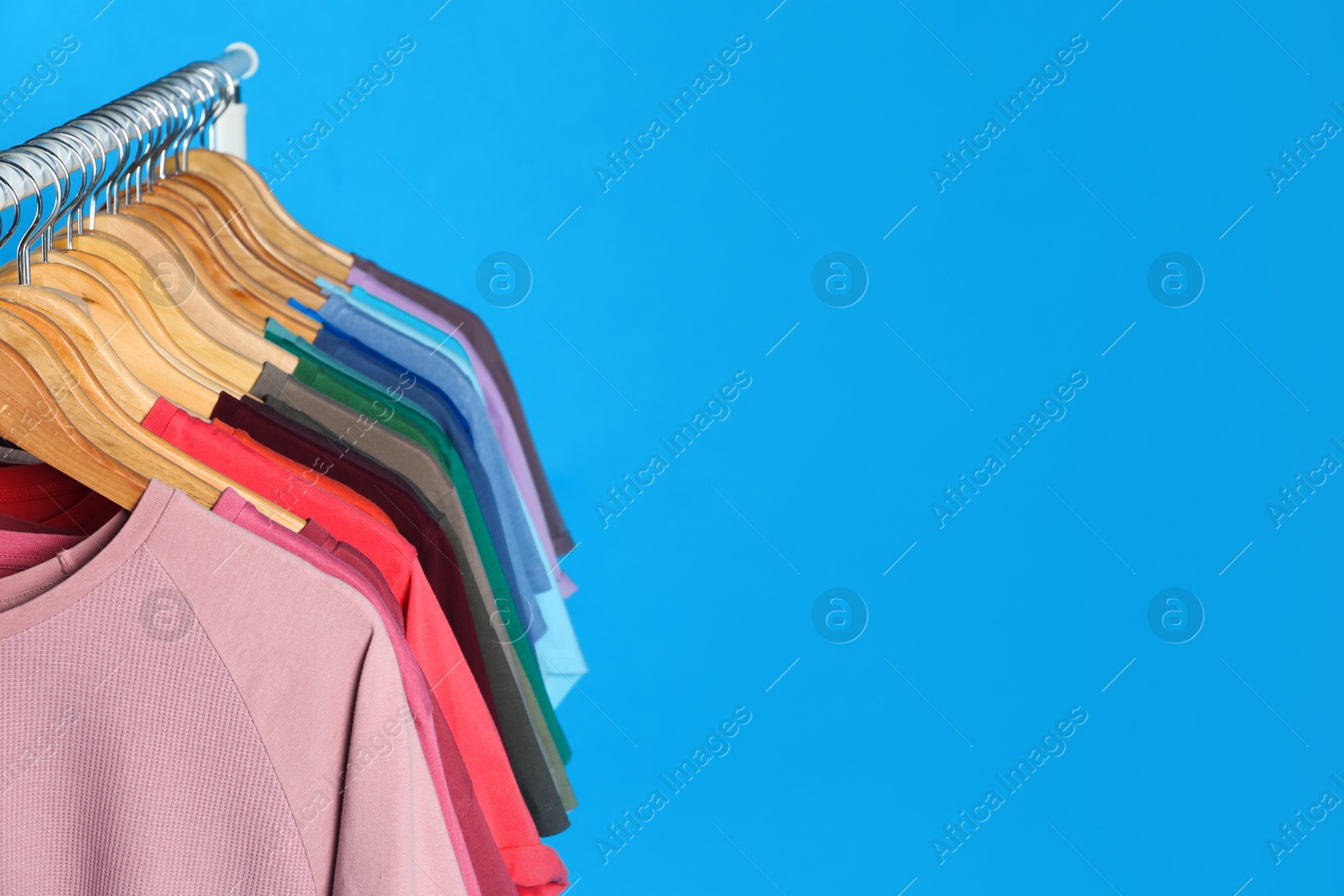 Photo of Colorful clothes hanging on rack against light blue background. Space for text