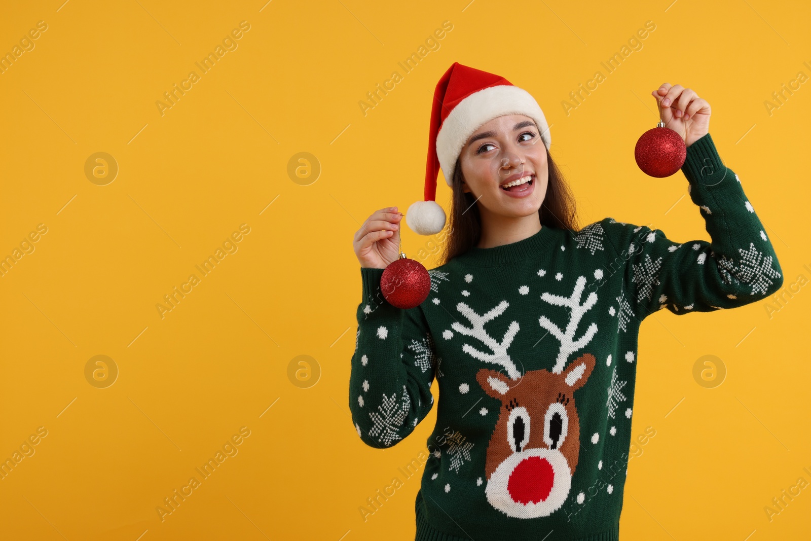 Photo of Happy young woman in Christmas sweater and Santa hat holding festive baubles on orange background. Space for text