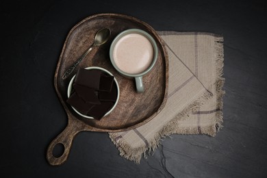 Cup of hot delicious cocoa served with chocolate on black table, flat lay